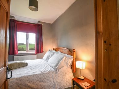 A bedroom with a double bed red curtains and a bedside table with a lamp at The Old Dairy Whitchurch Canonicorum near Charmouth