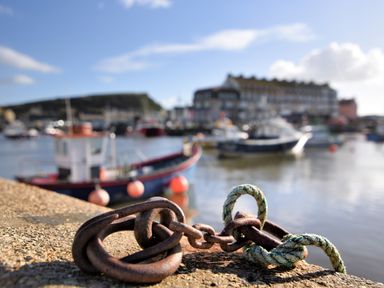 A close-up of a rusty chain and rope on a concrete ledge with boats and water in the background at The Old Dairy in Whitchurch Canonicorum near Charmouth