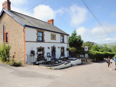 A roadside pub building with outdoor seating and two people standing nearby at The Old Dairy in Whitchurch Canonicorum near Charmouth