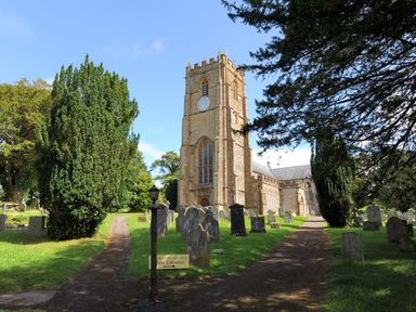 A stone church with a clock tower surrounded by gravestones and trees at The Old Dairy in Whitchurch Canonicorum near Charmouth