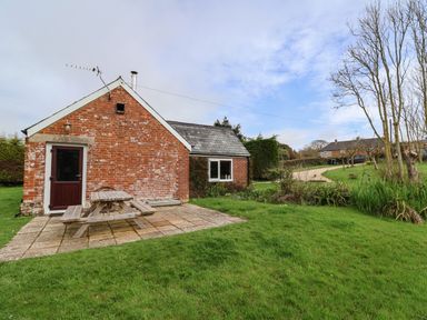 A backyard with a brick house a wooden picnic table on a patio and a grassy lawn at The Old Dairy in Whitchurch Canonicorum near Charmouth