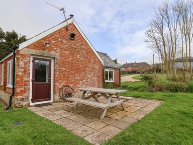 A brick house with a wooden door and windows with a wooden picnic table on a paved patio at The Old Dairy in Whitchurch Canonicorum near Charmouth