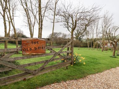 A wooden gate with a sign saying The Old Dairy surrounded by grass and trees at The Old Dairy Whitchurch Canonicorum near Charmouth