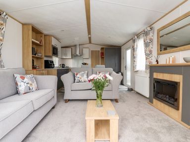 A living room with two sofas a coffee table with flowers and a fireplace at Silverdale View in East Heslerton near Sherburn