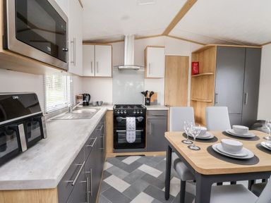 A kitchen with gray and white cabinets a stove and a dining table set with plates and glasses at Silverdale View in East Heslerton near Sherburn