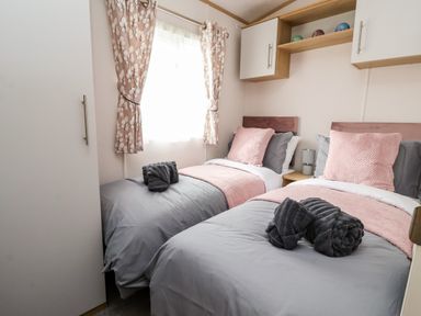 A bedroom with two single beds with pink and gray bedding and towels on each bed at Silverdale View in East Heslerton near Sherburn