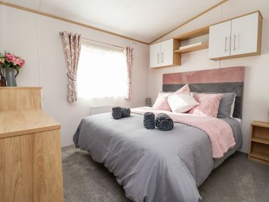 A bedroom with a bed with pillows and rolled towels a wooden cabinet and wall-mounted cupboards at Silverdale View East Heslerton near Sherburn