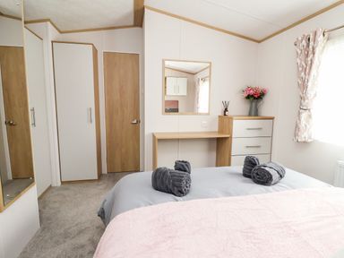 A bedroom with a bed, a desk, a mirror, a chest of drawers with flowers on top, and a wardrobe at Silverdale View in East Heslerton near Sherburn