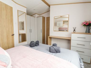 A bedroom with a bed holding folded towels a dresser with flowers a mirror and wardrobes at Silverdale View in East Heslerton near Sherburn