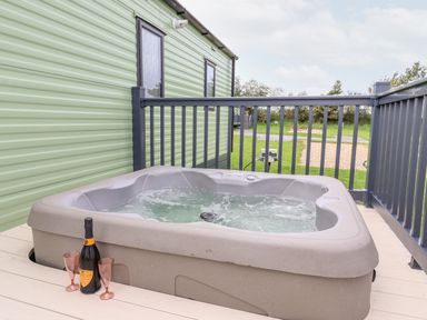 An outdoor hot tub on a wooden deck with two pink glasses and a bottle next to it at Silverdale View in East Heslerton near Sherburn