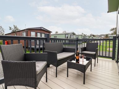 A patio with wicker chairs and a table holding a bottle and glasses at Silverdale View in East Heslerton near Sherburn