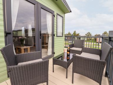 A balcony with four wicker chairs and a glass table with a bottle and glass in a green mobile home park at Silverdale View in East Heslerton near Sherburn