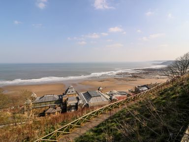 A coastal view with a beach and buildings below a grassy hillside at Silverdale View in East Heslerton near Sherburn
