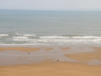 A sandy beach with two people standing near the shoreline and waves in the sea at Silverdale View in East Heslerton near Sherburn