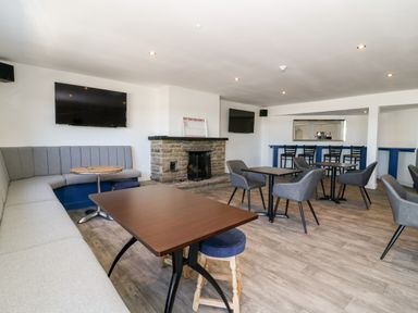 A lounge area with tables chairs a stone fireplace and two wall mounted televisions at Silverdale View in East Heslerton near Sherburn