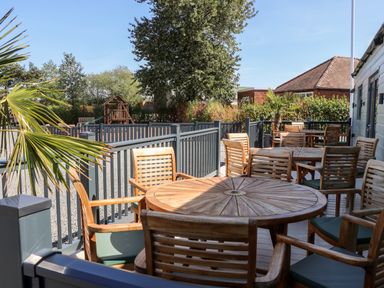 An outdoor seating area with wooden tables and chairs near a playground and trees at Silverdale View in East Heslerton near Sherburn
