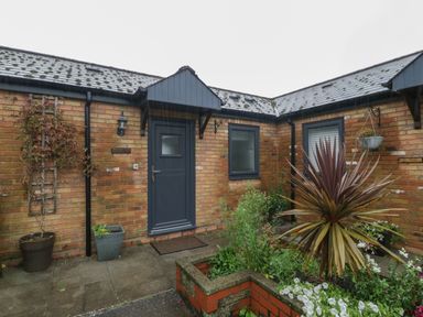 A brick exterior with a blue door and windows surrounded by plants and flowers at Myrtle Cottage in St Brides-Super-Ely