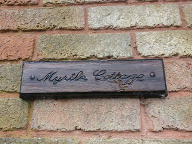 A wooden sign with the text Myrtle Cottage on a brick wall at Myrtle Cottage in St Brides-Super-Ely