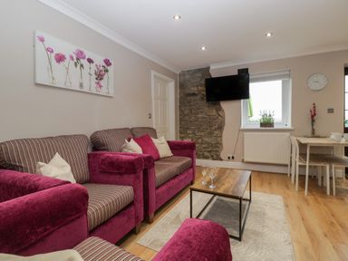 A living room with pink armchairs a wooden coffee table a wall-mounted TV and a dining table at Myrtle Cottage in St Brides-Super-Ely