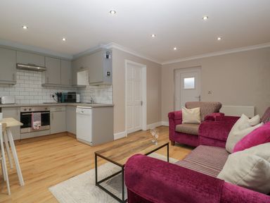 A living area with purple sofas and a wooden coffee table beside a kitchen with grey cabinets and white appliances at Myrtle Cottage in St Brides-Super-Ely