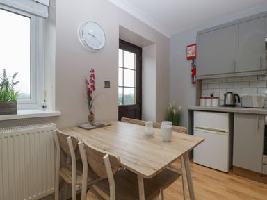 A kitchen with a wooden dining table and chairs near a window and a door at Myrtle Cottage in St Brides-Super-Ely