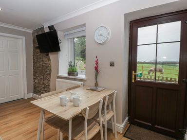 A dining area with a wooden table and four chairs next to a window and a door overlooking a grassy field with horses at Myrtle Cottage in St Brides-Super-Ely