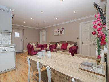 A dining area with wooden table and chairs and a living room with pink armchairs and sofa at Myrtle Cottage in St Brides-Super-Ely