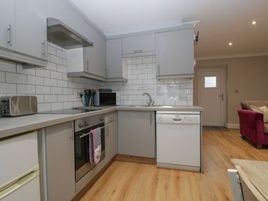 A kitchen with gray cabinets white tiled backsplash stainless steel oven and dishwasher and wooden floor at Myrtle Cottage in St Brides-Super-Ely