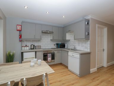 A kitchen with grey cabinets a wooden dining table and chairs a dishwasher and microwave at Myrtle Cottage in St Brides-Super-Ely