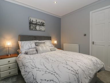 A bedroom with a bed with patterned bedding two bedside tables and lamps and a door at Myrtle Cottage in St Brides-Super-Ely