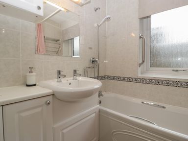 A bathroom with a sink and a bathtub next to a frosted window at Myrtle Cottage in St Brides-Super-Ely
