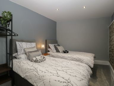 A bedroom with two single beds pillows bedside table lamp and open wardrobe at Myrtle Cottage in St Brides Super Ely