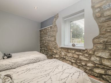 A bedroom with two single beds next to a stone wall and a window at Myrtle Cottage in St Brides-Super-Ely