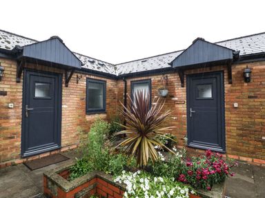 A courtyard with two black doors and multiple windows around a planter with various plants and flowers at Myrtle Cottage in St Brides-Super-Ely