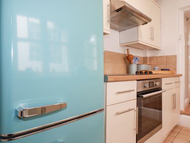 A kitchen with a turquoise fridge stove with a wooden countertop and white cabinets at Waves End in Mevagissey