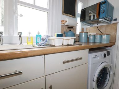 A kitchen countertop with soap dispensers a dish rack kettle storage canisters microwave and a washing machine at Waves End in Mevagissey