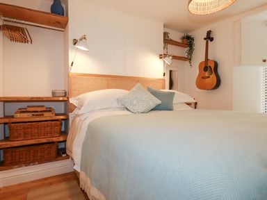 A bedroom with a bed a guitar on the wall and wooden shelves with wicker baskets at Waves End in Mevagissey