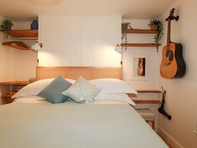A bedroom with a bed with pillows and a guitar hanging on the wall at Waves End in Mevagissey