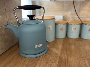A kitchen counter with a blue kettle and matching blue containers with wooden lids at Waves End in Mevagissey