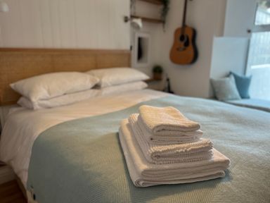 A bed with white pillows and folded towels with a guitar on the wall in a bedroom at Waves End in Mevagissey