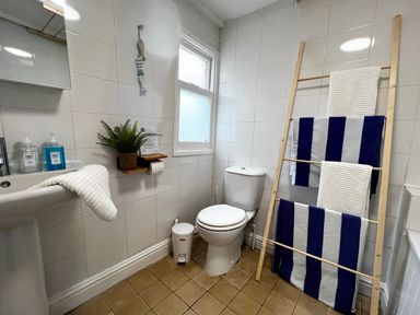 A bathroom with a toilet sink mirror window and towel rack holding striped towels at Waves End in Mevagissey