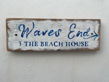 A wooden sign with the text Waves End 3 The Beach House attached to a white wall at Waves End in Mevagissey