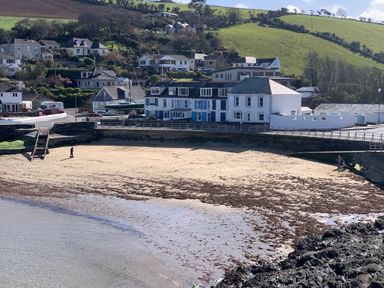 A sandy beach with seaweed and people near a seaside village with houses and green hills in the background at Waves End Mevagissey