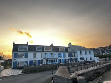 A row of houses with blue and white shutters near a stone wall and a car on the street at Waves End in Mevagissey