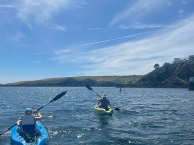People kayaking on the water near a coastline with hills and houses in Mevagissey