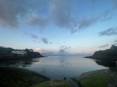 A coastal bay with houses on the left cliffs and rocky shorelines on both sides at Waves End in Mevagissey