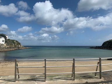 A beach with sand and sea with a metal railing in the foreground at Waves End in Mevagissey