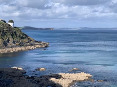 A rocky coastline with a white round building on a cliff overlooking the sea at Waves End in Mevagissey