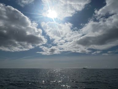 A seascape with sunlight reflecting on water and clouds in the sky at Waves End in Mevagissey