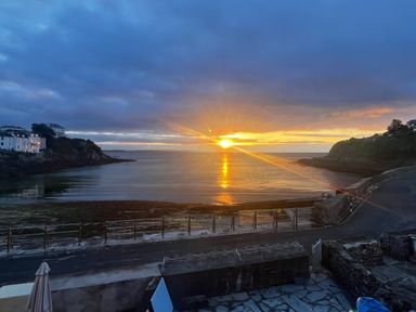 A coastal scene with a sunset over the sea and houses on cliffs at Waves End in Mevagissey